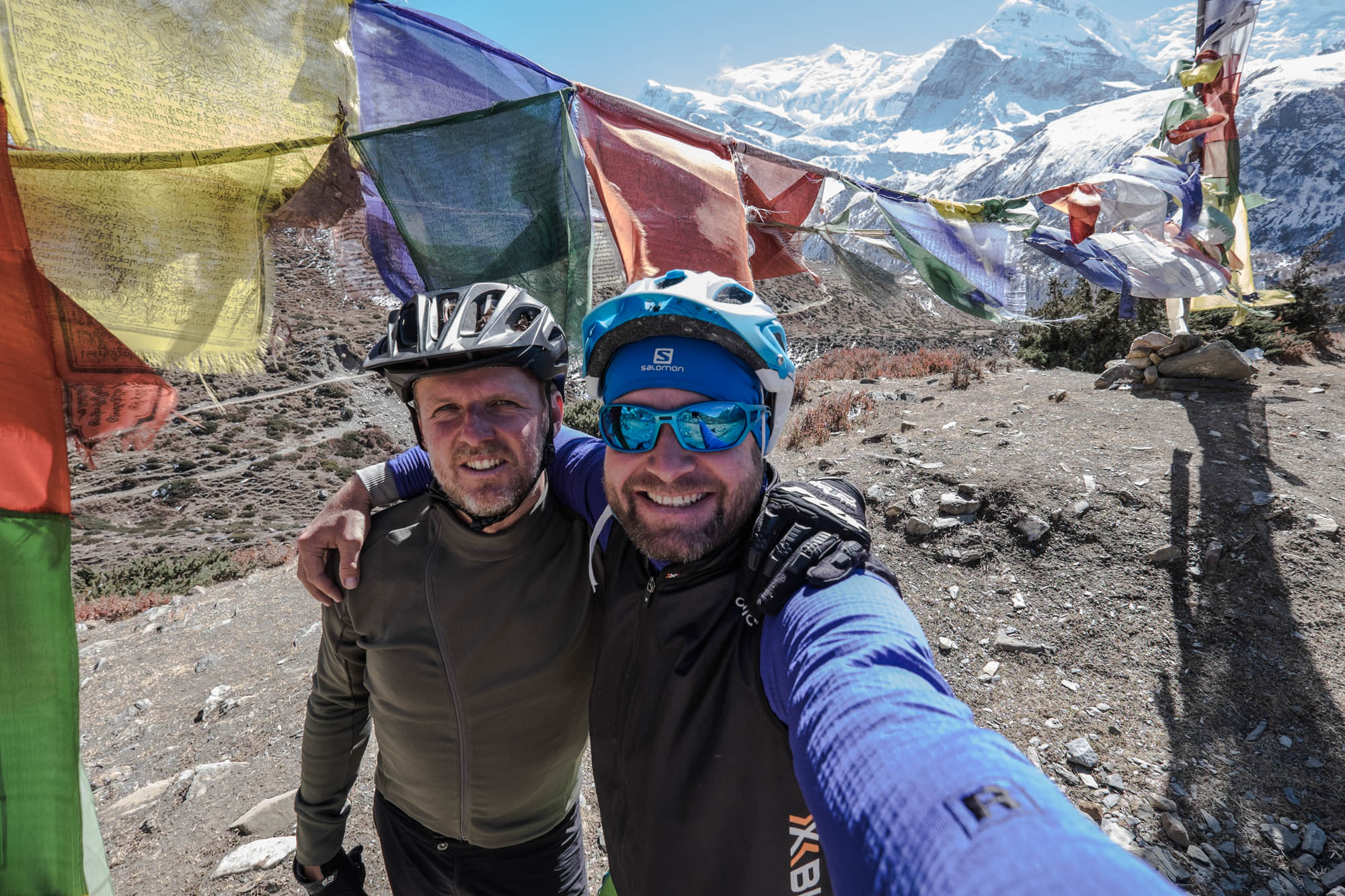 Selfie von Jens Vögele und Andreas Kern neben buddhistischen Gebesfahnen und vor dem Panorama des Himalaja.